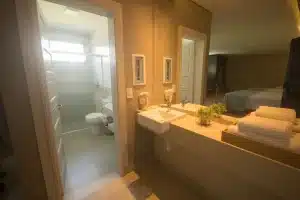 Banheiro e lavabo moderno nas acomodações no Grand Carimã Hotel em Foz do Iguaçu, com bancada clara e iluminação embutida.